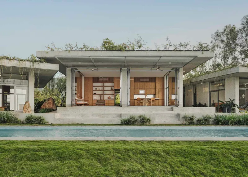 Poolside view of the concrete pavilion with folding glass doors opening to the kitchen and dining areas