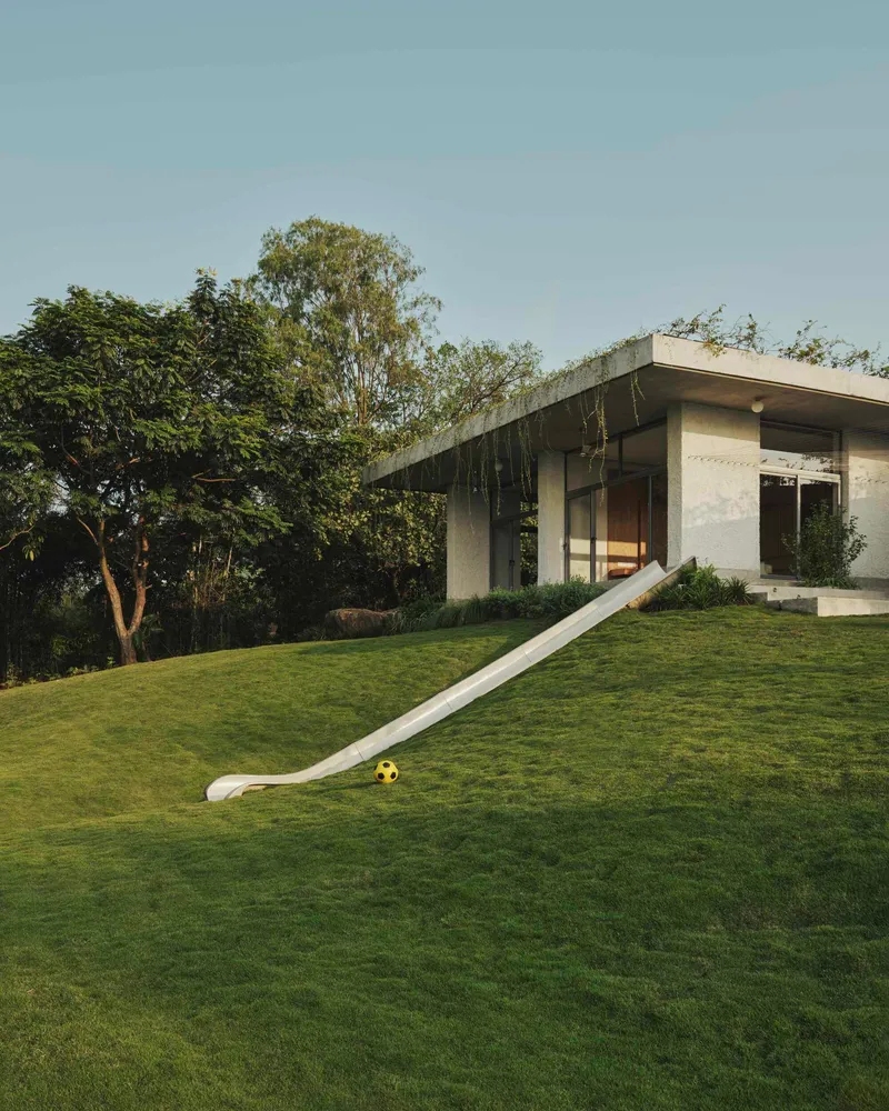 Planted roof over the concrete volumes with a white slide descending the lawn and a soccer ball