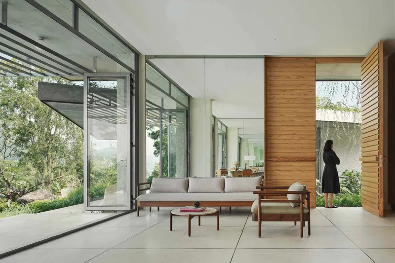 Open living space with folding glass walls, timber feature wall, and a figure standing by the courtyard