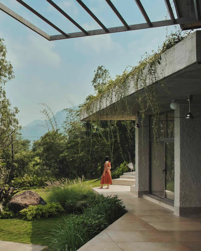 Covered walkway with concrete pergola beams and planted roof edges framing a view toward distant mountains