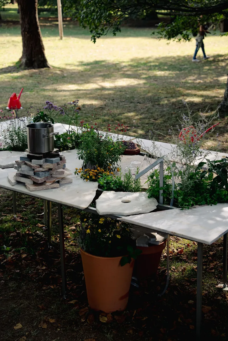 White cast table with potted plants and a stacked brick cooking platform in the park