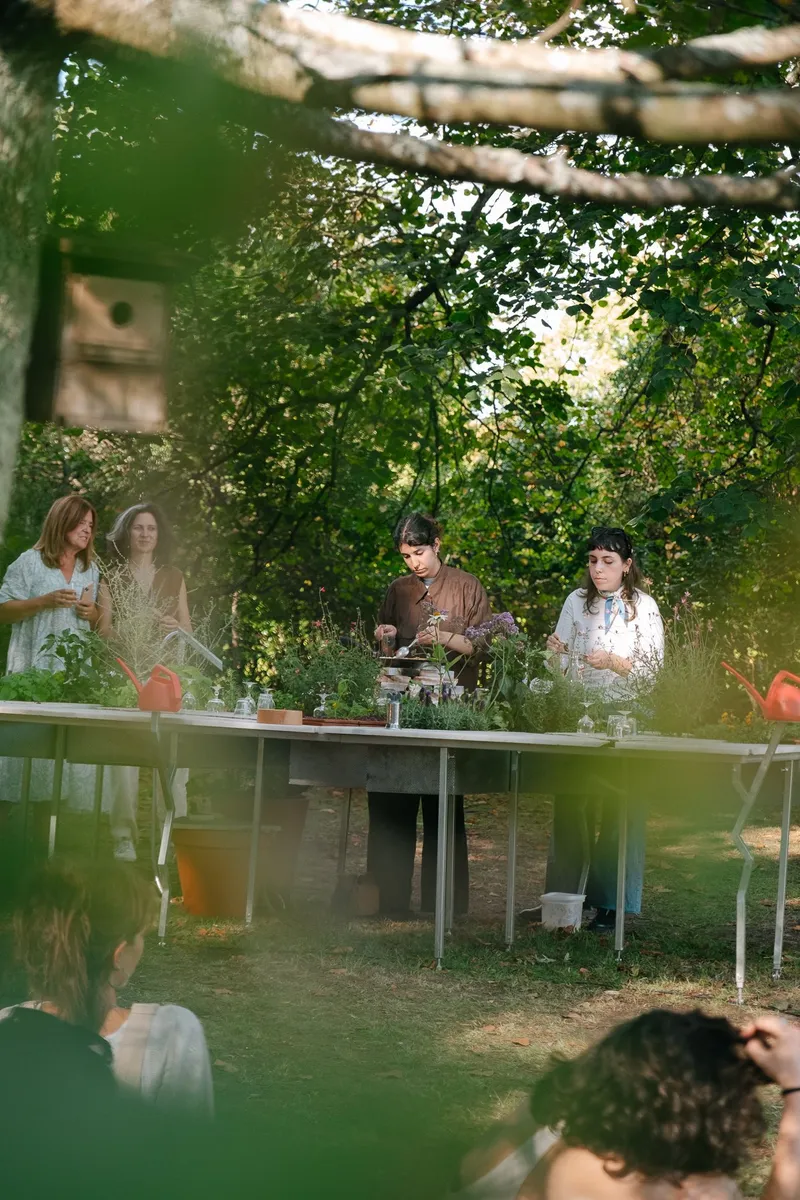 Outdoor table beneath a vine-covered timber pergola with people gathered in dappled afternoon light
