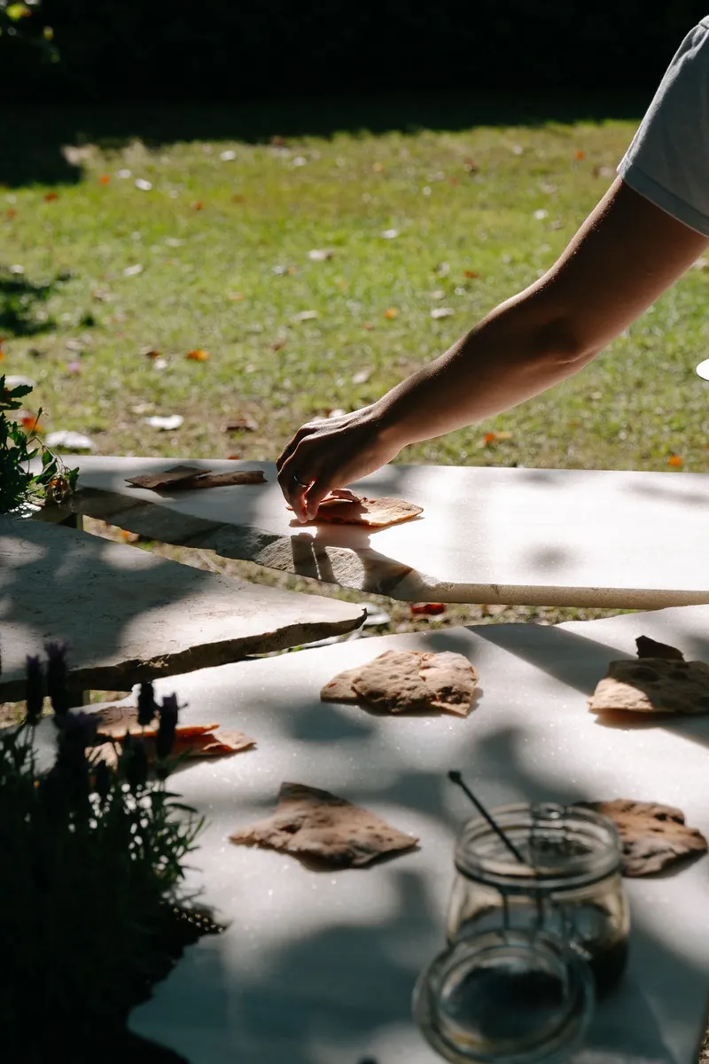 Hand arranging flatbread on a white painted table surface with flower petals scattered across the lawn