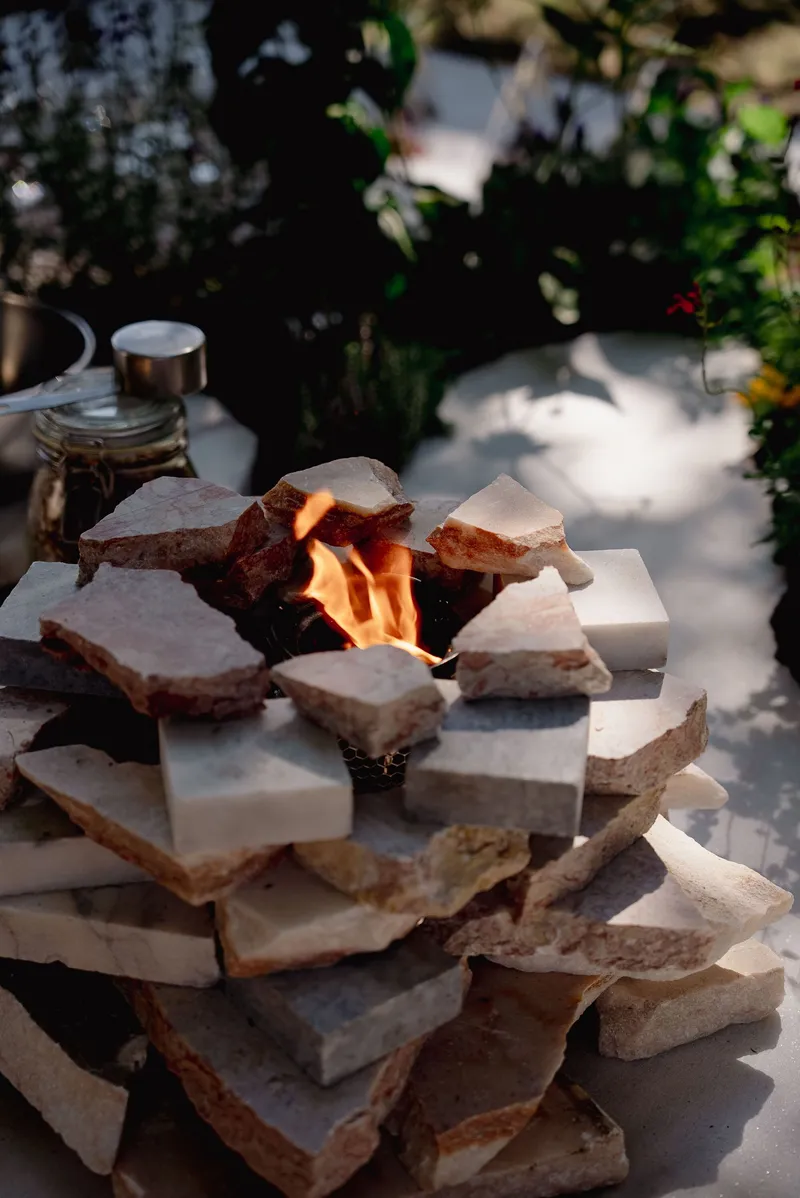 Stacked stone fire feature with active flame on an outdoor table surrounded by plants and glassware