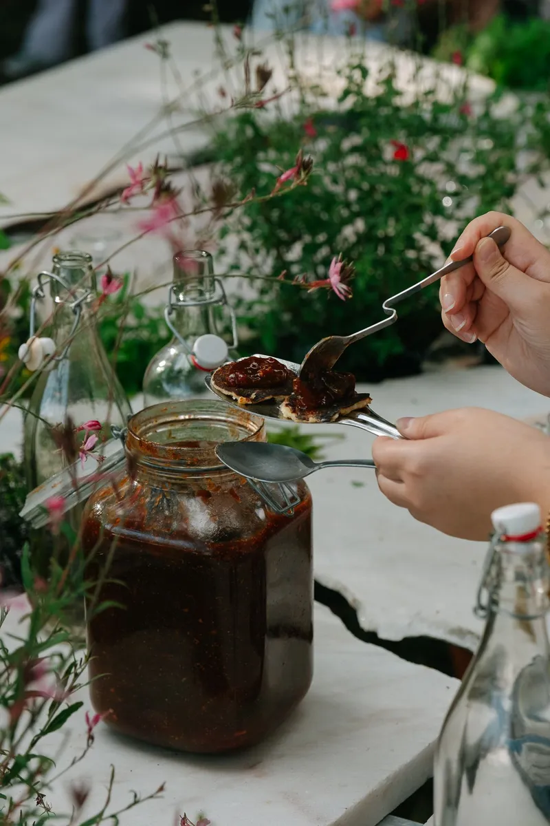 Hand holding a fork over a glass jar of preserve with wildflowers in the background