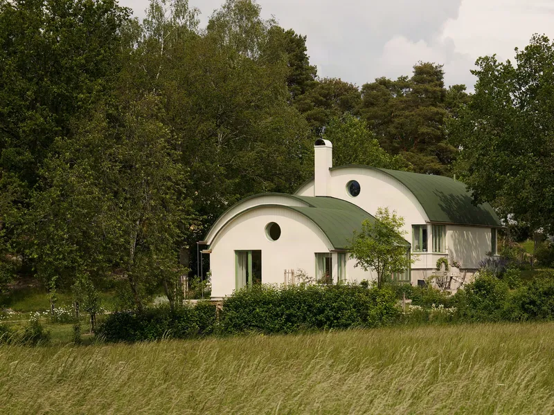 White vaulted volumes with green barrel roofs and circular windows set in a meadow landscape