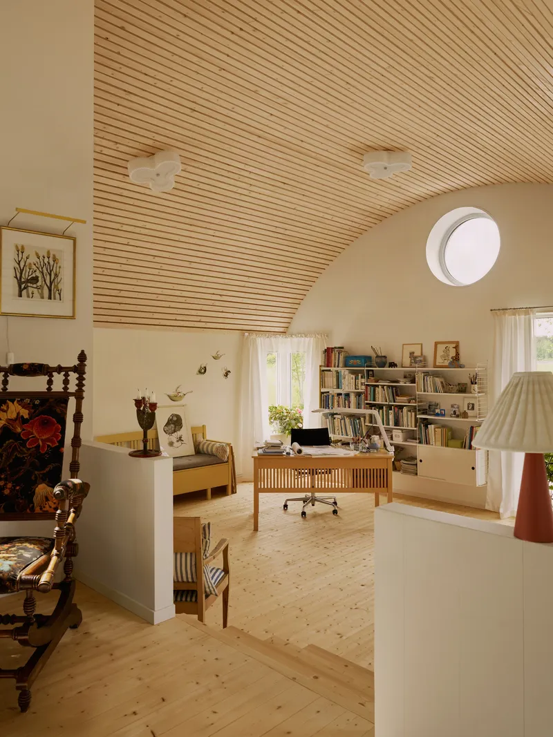 Vaulted wooden slat ceiling over pine floor study with circular skylight and low bookshelves