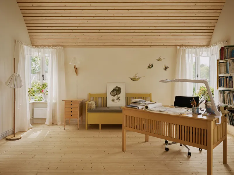 Home office with wooden desk and slatted ceiling panel beneath two curtained windows