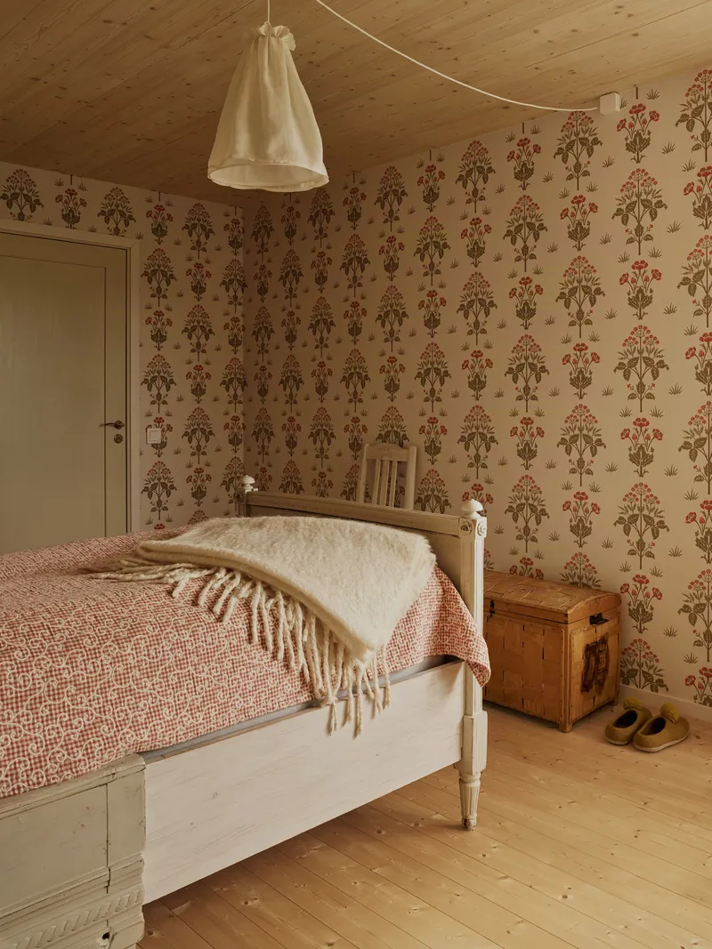Bedroom corner showing botanical wallpaper, timber ceiling planks and a fabric pendant lamp overhead