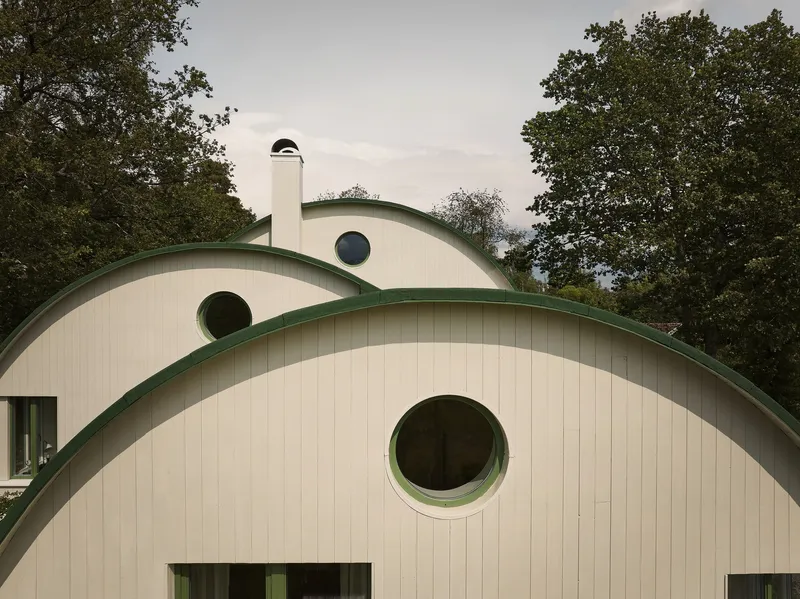 Arched facades with vertical paneling and green trim punctuated by circular windows beneath an overcast sky