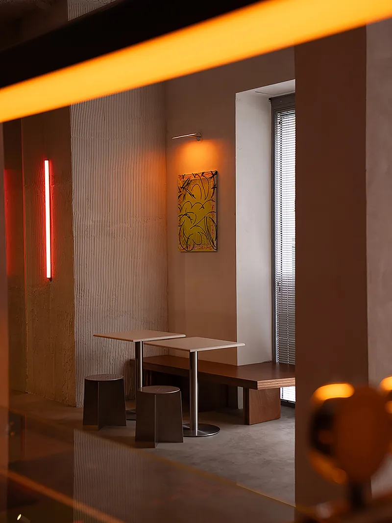 Seating nook with ribbed wall panels, vertical orange tube light and filtered window at dusk