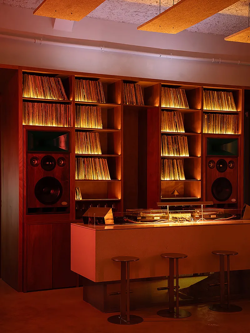 Listening bar with vinyl shelves and integrated speakers beneath acoustic ceiling panels under warm lighting