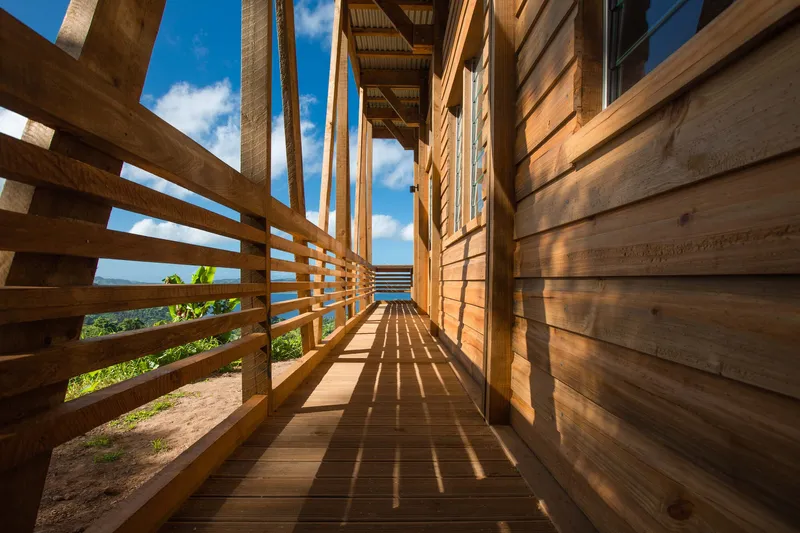 Narrow exterior walkway with horizontal timber railings casting afternoon shadows on the deck
