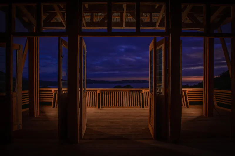 Interior view through timber frame and glass doors to the deck railing at dusk