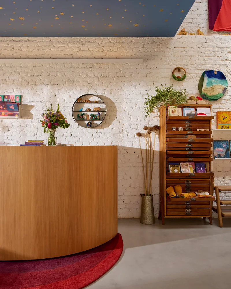 Interior view of curved timber service desk against whitewashed brick wall with round mirror and painted blue ceiling