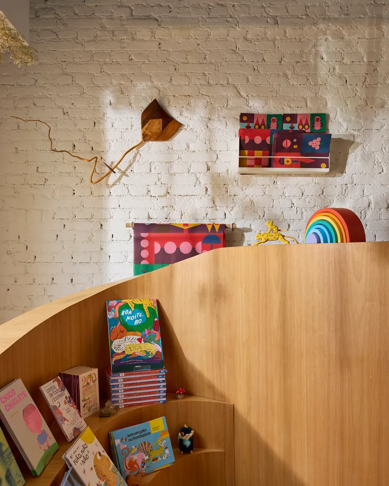 Close-up of stepped timber display shelving against exposed whitewashed brick wall with mounted wooden kite and artwork