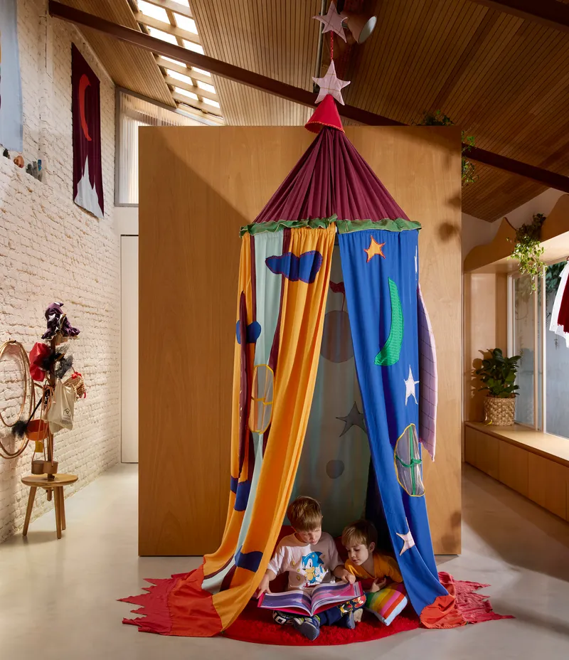 Fabric play tent with celestial appliqués in double-height space with slatted timber ceiling and whitewashed brick wall