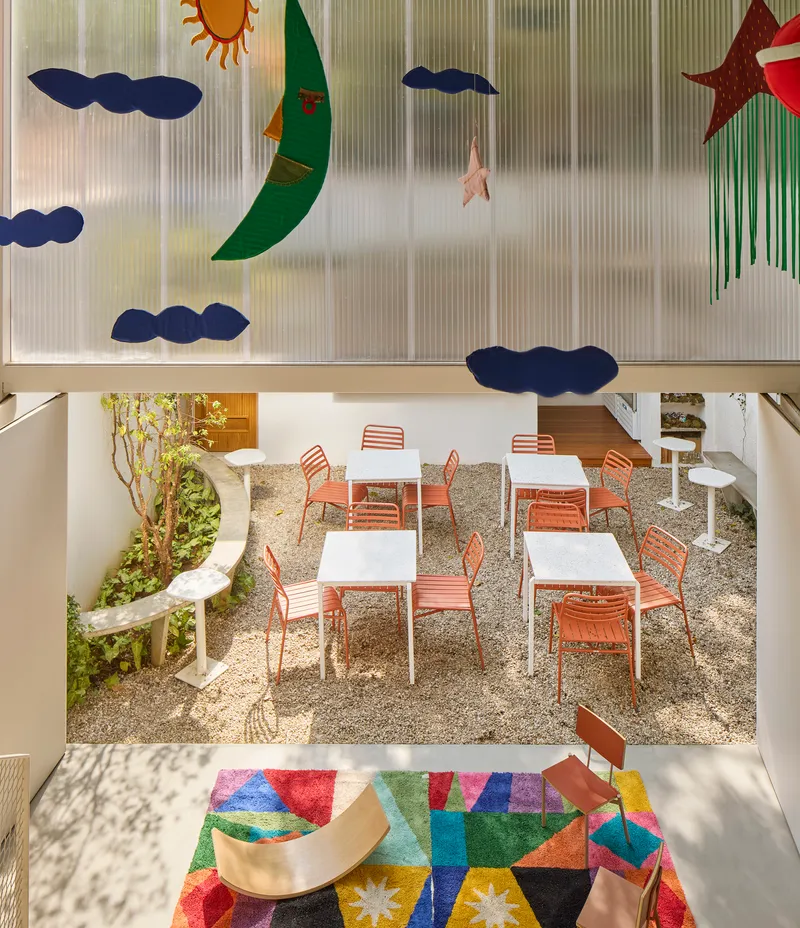 Double-height view through translucent wall with celestial appliques into gravel courtyard with orange chairs
