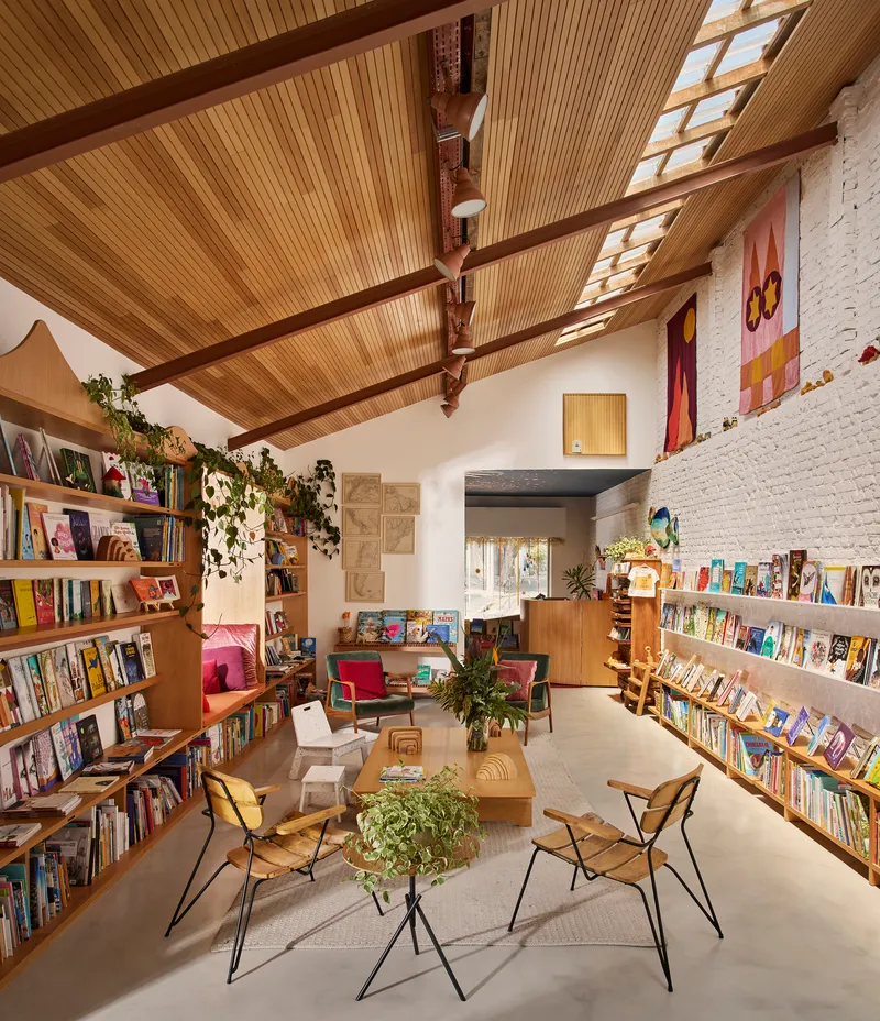 Interior of a bookshop with timber-slatted ceiling, exposed beams, skylights and trailing vines