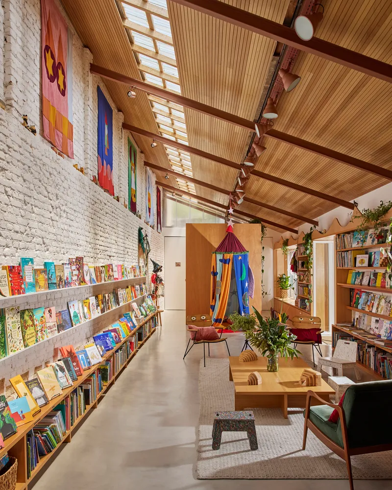 Long view through the bookshop showing timber ceiling, painted brick wall and central reading area