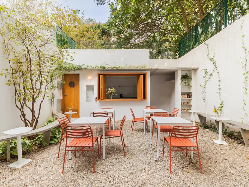 Outdoor courtyard with gravel flooring, coral chairs, timber service window and planted tree