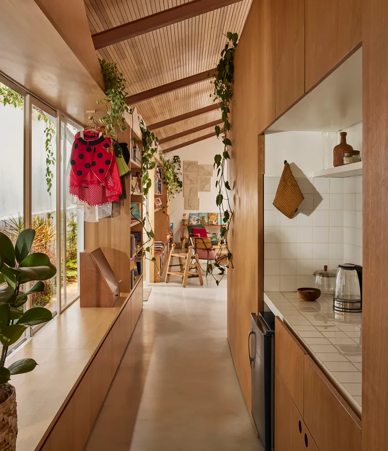 Galley corridor with timber slat ceiling and hanging plants leading toward kitchen with white tile