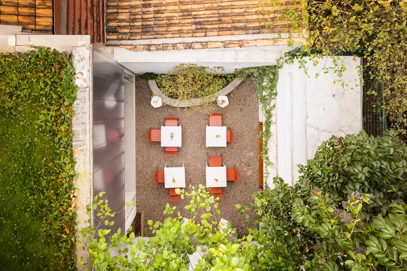Overhead view of gravel courtyard with orange dining chairs and curved planted bed with white bench
