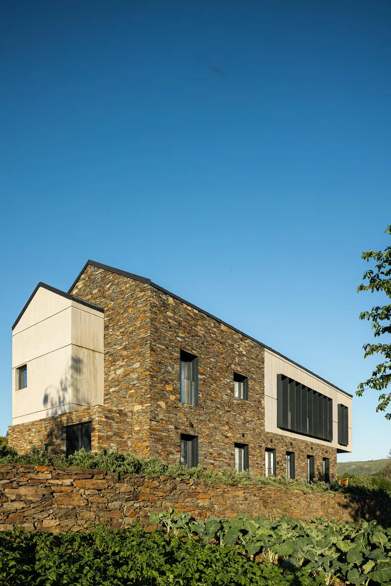 Stacked stone walls contrasting with white rendered and timber clad volumes under clear sky