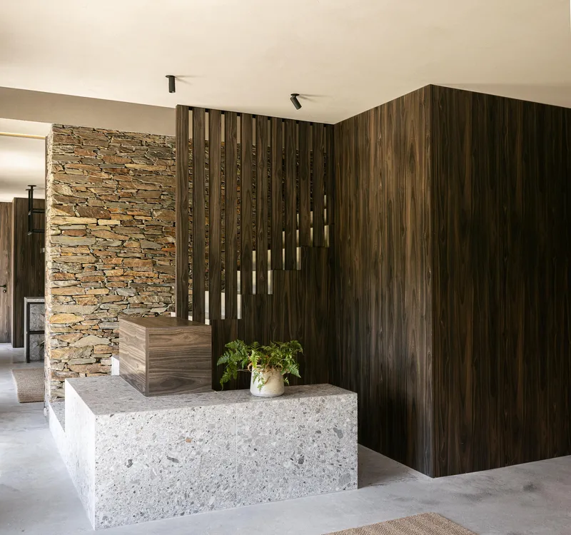 Interior entry with stacked stone wall and vertical timber slat screen beside a terrazzo reception counter