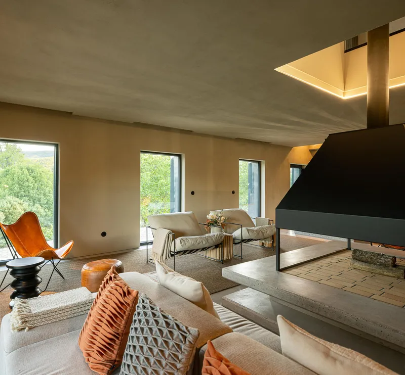 Living room with polished concrete steps leading to fireplace beneath a skylight and plastered walls