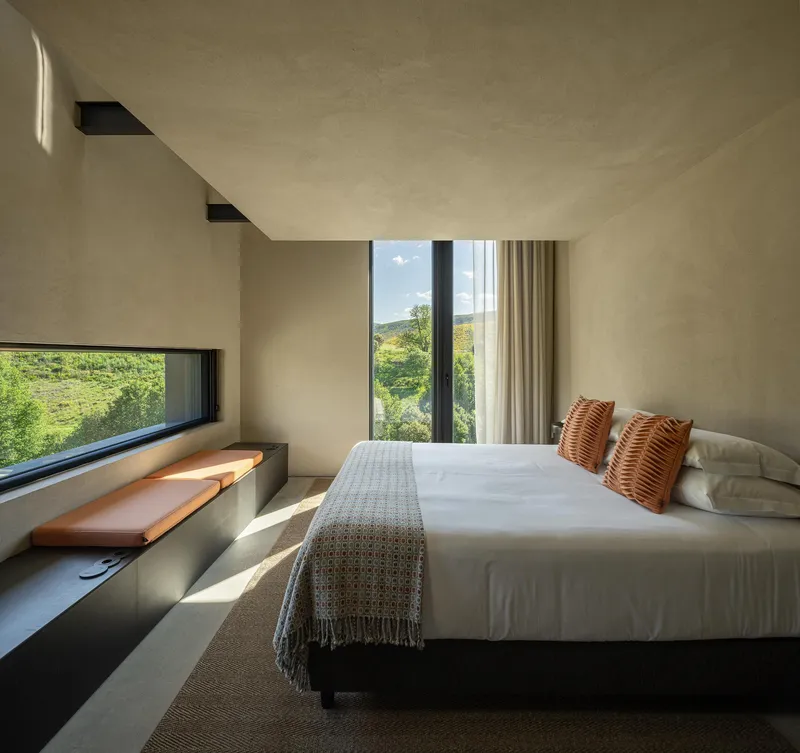 Bedroom with concrete window seat and full-height glazing framing views of the green hillside