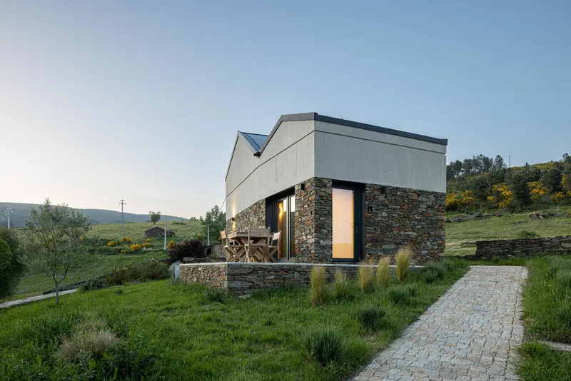 Hillside residence with stone plinth and concrete upper volumes at twilight with cobbled path