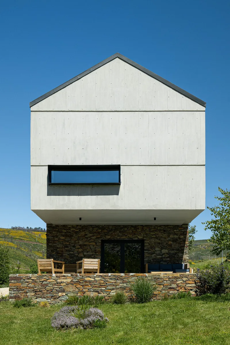 Front elevation showing the gabled form with horizontal window and stacked stone base under clear blue sky