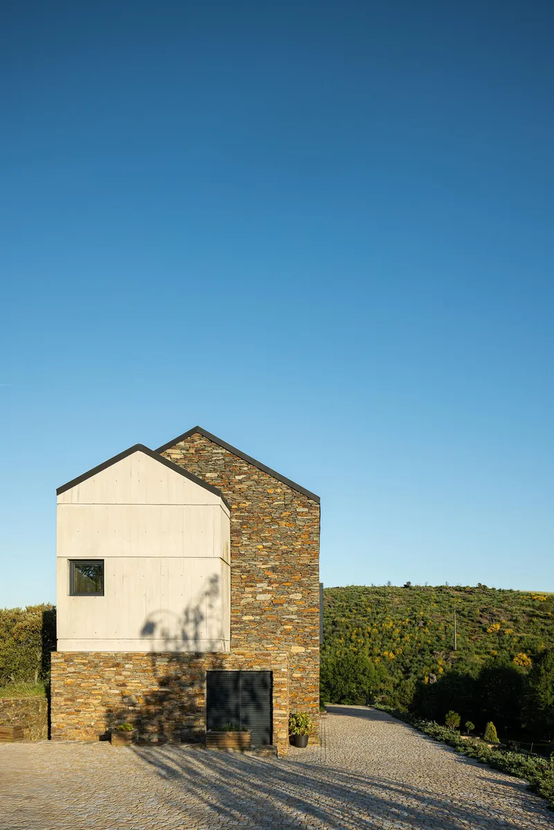 Side elevation at dusk showing the contrast between pale paneled and stone-clad gable walls with tree shadow