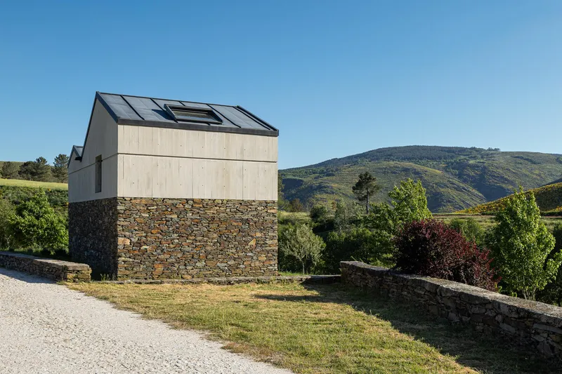 Two-story structure with pale timber upper volume and fieldstone base set against rolling hills