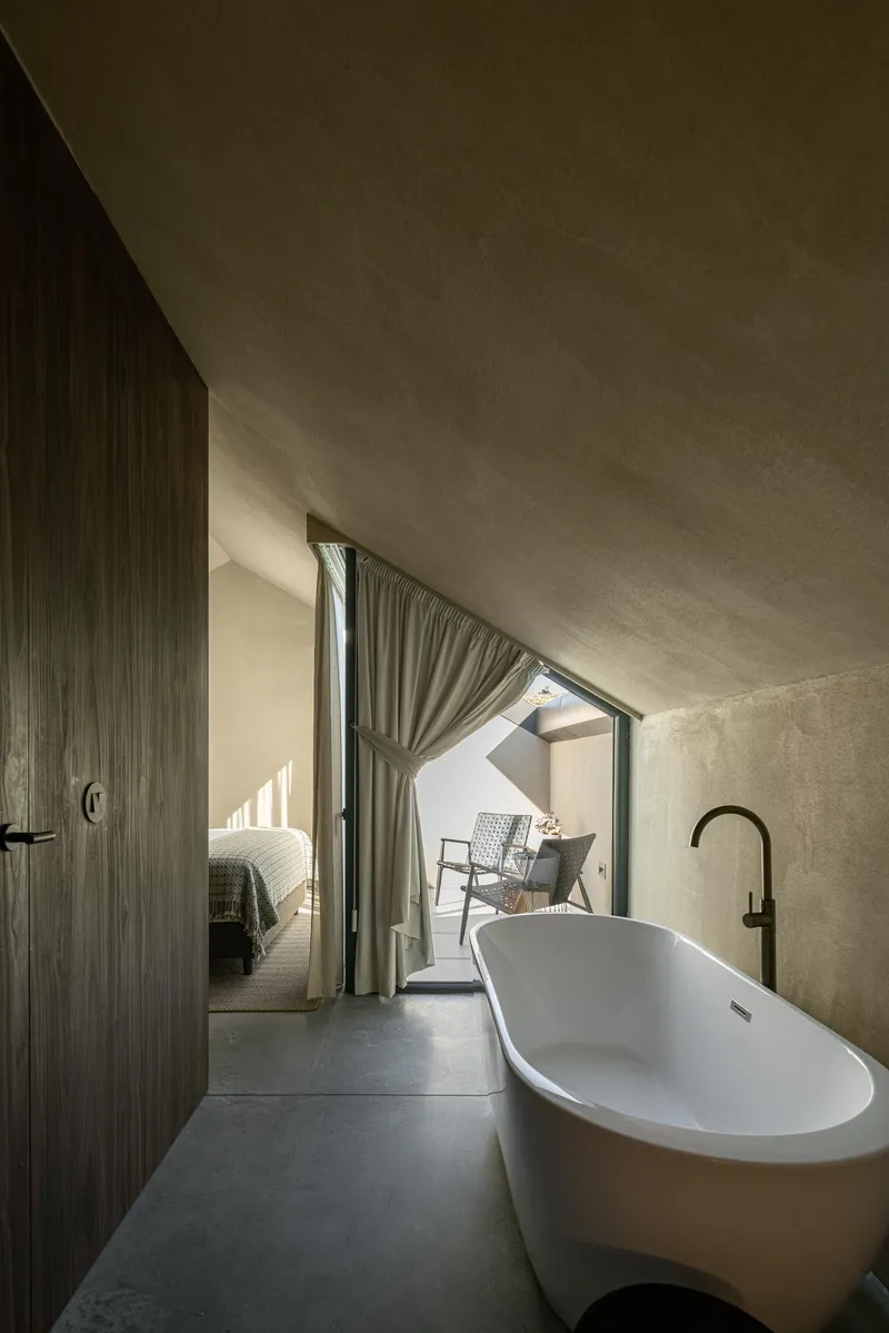 Bathroom with curved plaster ceiling and freestanding bathtub opening to curtained terrace with sunlight
