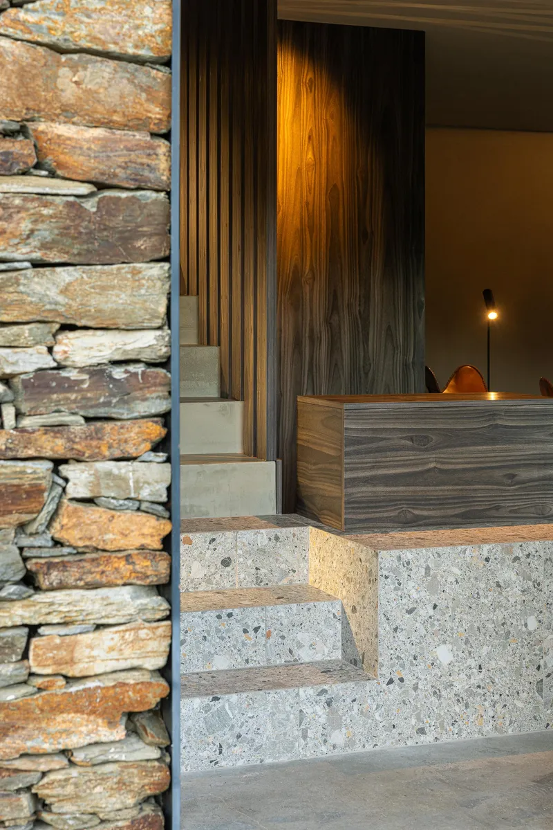 Polished concrete steps leading to a wood reception desk beside a rough stone wall with warm uplighting