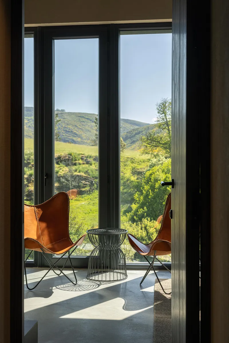 Glass doors opening from interior to a terrace with leather butterfly chairs overlooking green valley hillsides