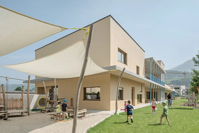 Corner view showing fabric shade canopy over a play area with children and adjacent glass facade