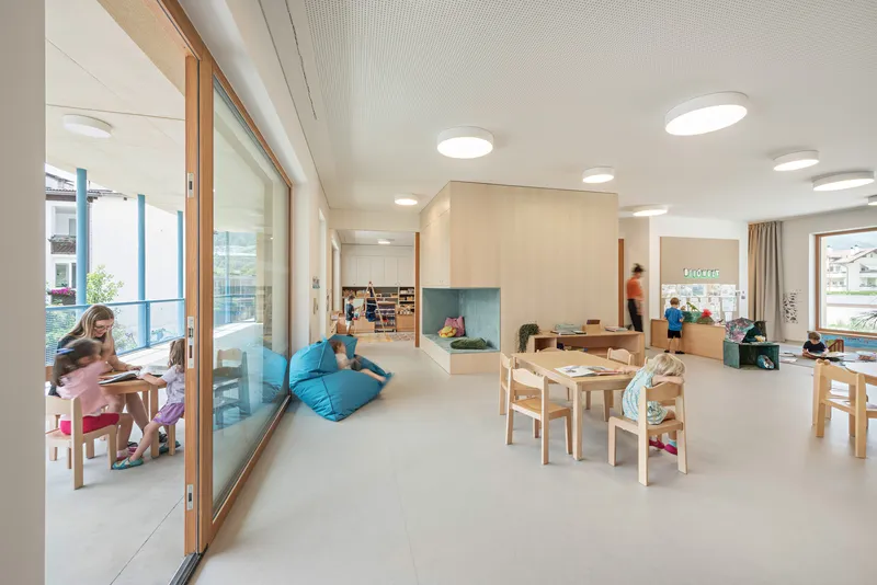 Interior room with light timber millwork and children at play tables beneath round ceiling fixtures