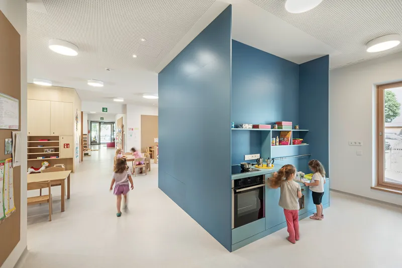 Freestanding blue kitchen volume with integrated shelving and two children at the counter