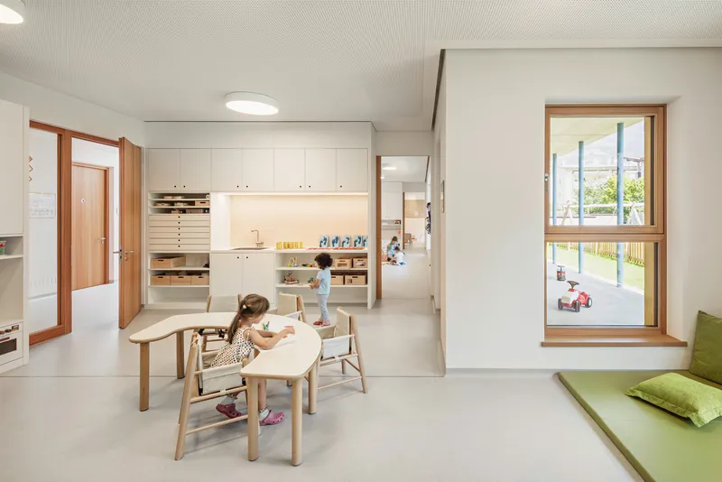 White classroom with timber-framed storage units and children at low tables under a ribbed ceiling