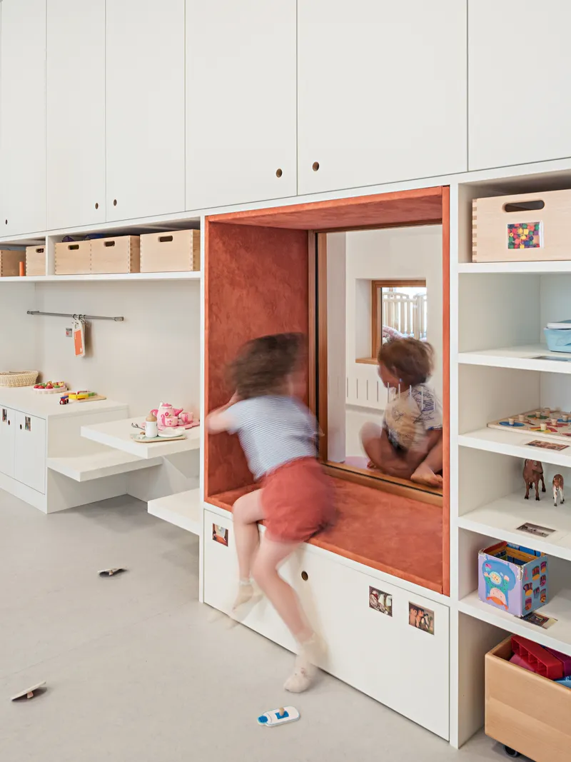 Built-in storage niche with orange plywood interior and children climbing through the opening