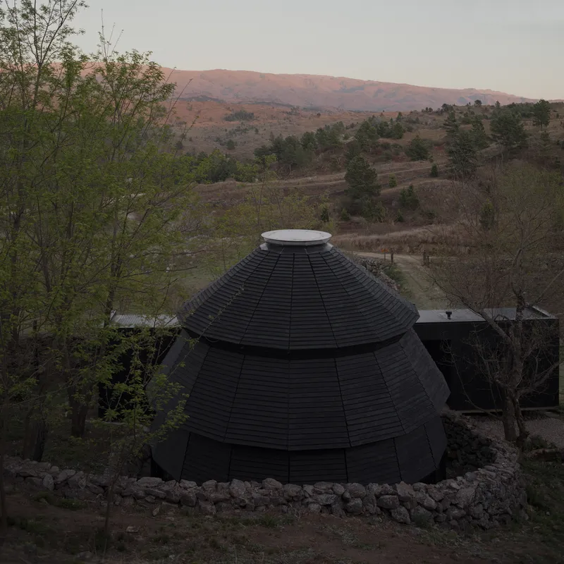 Aerial view of the black shingled dome with circular skylight surrounded by rolling hillside at dusk