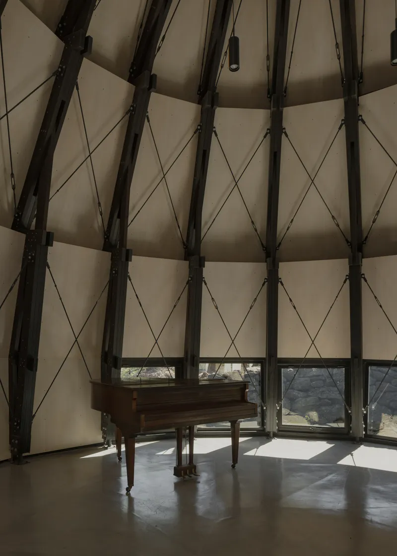 Interior of the conical volume with exposed steel beams, cable bracing and a piano on polished concrete