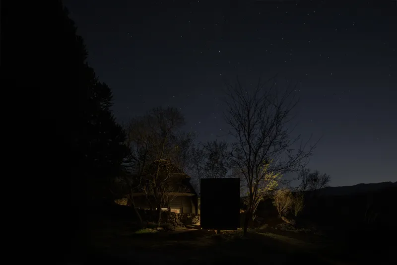 Night view of illuminated dome and timber box volumes under a star-filled sky