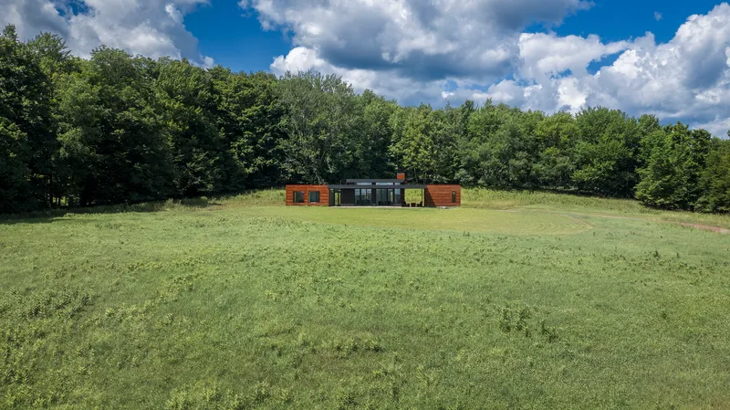 Long view across the sloping meadow with the linear residence anchored against the forest edge