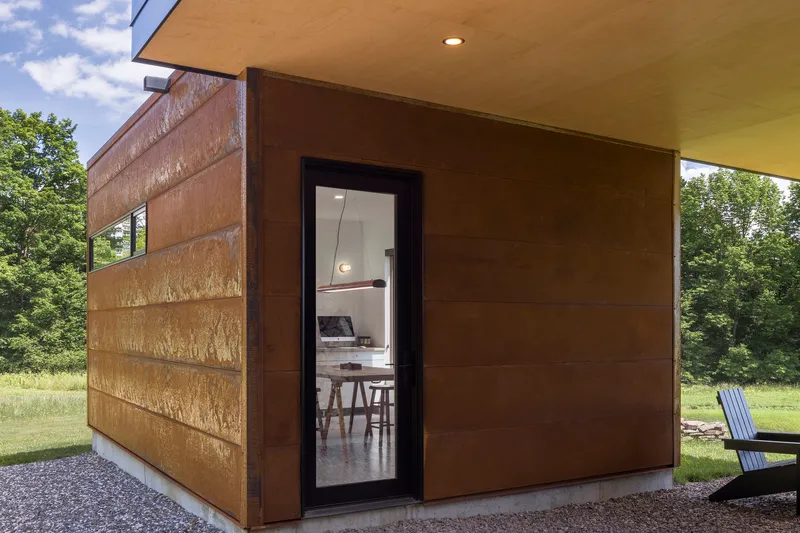 Corner detail of weathered steel panels meeting horizontal cedar siding beneath a deep roof overhang