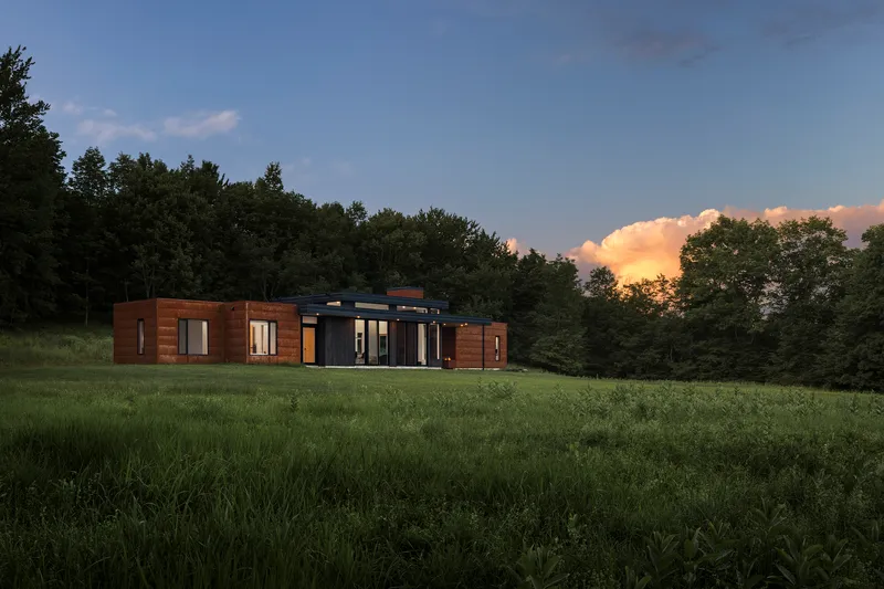Oblique view of the residence with interior lights glowing at dusk beneath gathering storm clouds