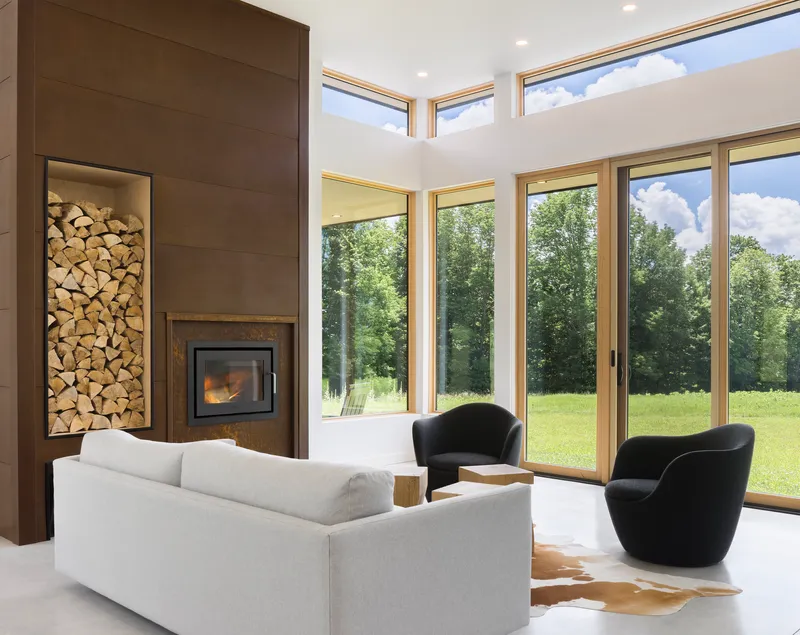 Living room with double-height glazing, built-in wood storage alcove, and fireplace beneath clerestory windows